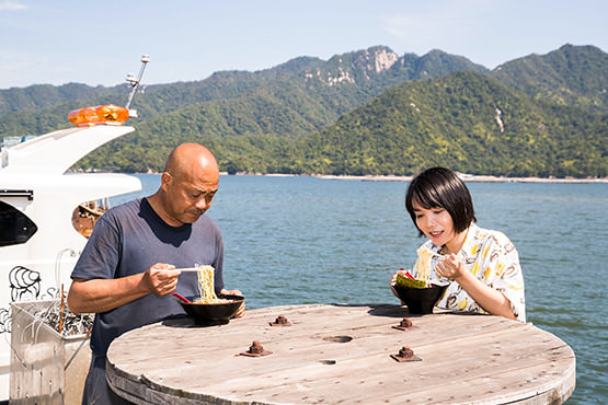 大野瀬戸の心地よい風のなか牡蠣ラーメンを食べる島田研究員と山根研究員